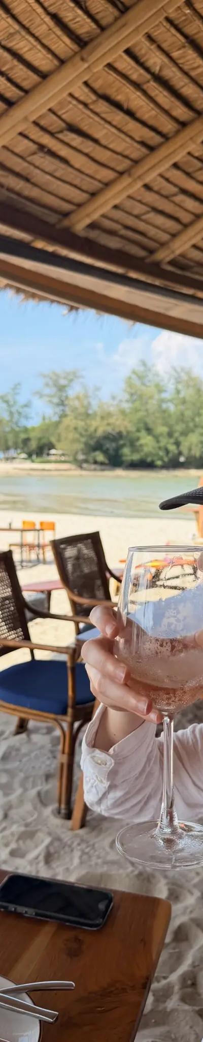 OPH trucker hat with a glass of wine at a thatched-roof beach restaurant in Thailand