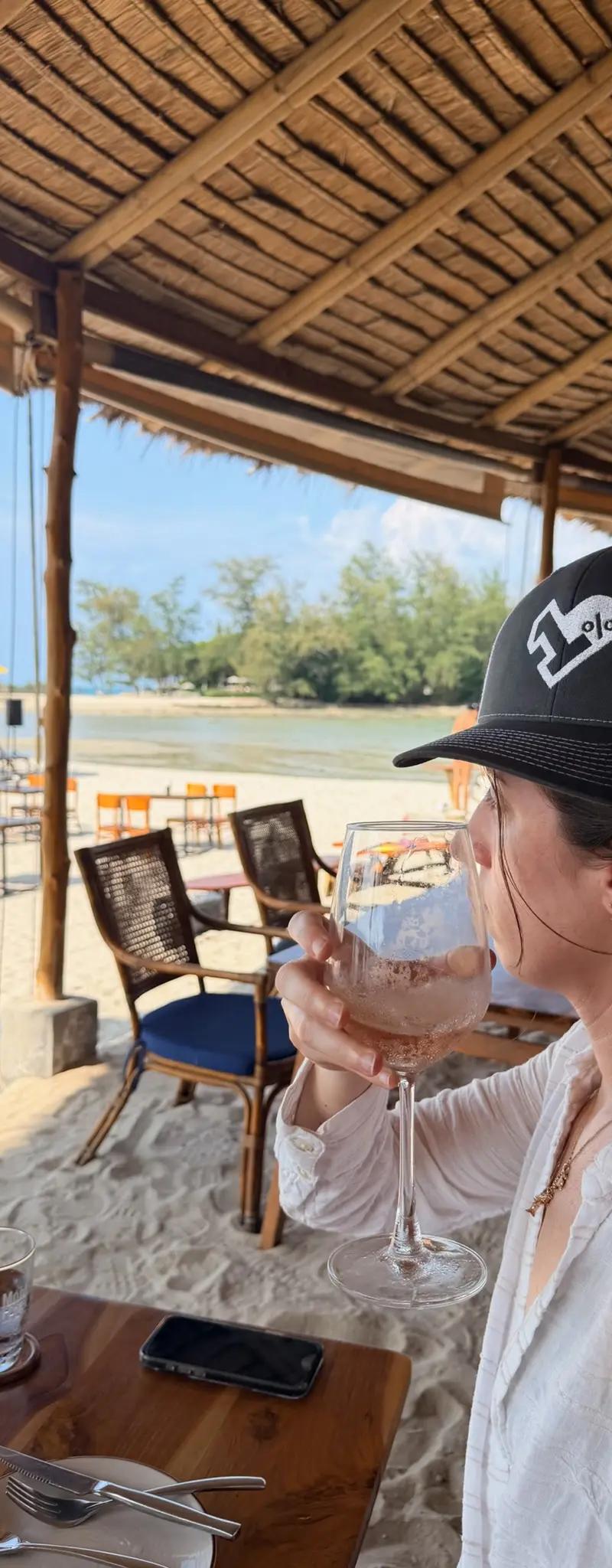 OPH trucker hat with a glass of wine at a thatched-roof beach restaurant in Thailand